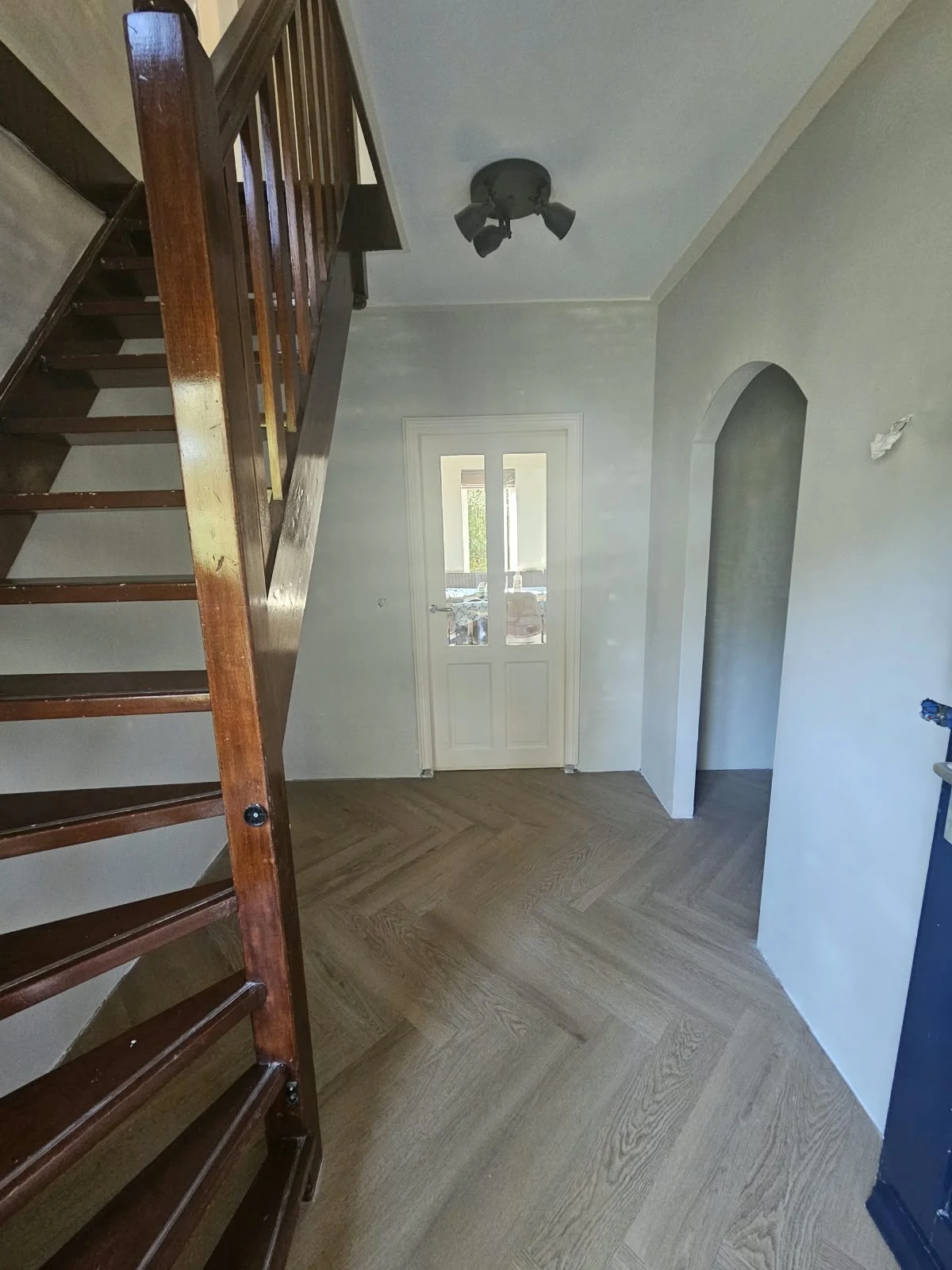 Gestucte hal met ronde doorgang en houten trap